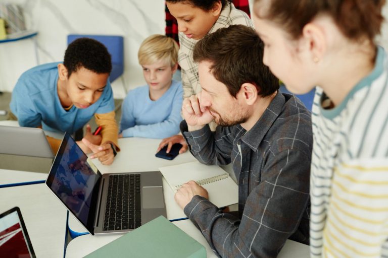 high-angle-portrait-male-teacher-with-diverse-group-kids-using-laptop-school
